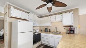 Une cuisine de taille réduite, avec des meubles blancs, un réfrigérateur, une cuisinière, un four à micro-ondes et un évier.