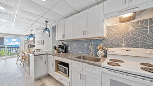 Una cocina moderna con armarios blancos, un lavamanos de acero inoxidable y un microondas integrado.
