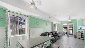 Ein Zimmer mit Esstisch, Stühlen, einer Couch, einem Fernseher und einem Deckenventilator.
