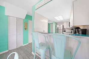 A kitchen with white cabinets, a countertop, and a hanging sign. There are two light blue chairs.