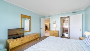 Une chambre à coucher comprenant un lit, une commode, un téléviseur et une porte donnant sur une salle de bain.