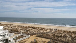Une vue sur la plage, avec un bâtiment blanc doté d’une zone délimitée par une clôture et une plage de sable au premier plan.