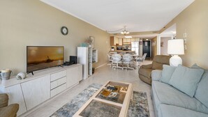 Un salon avec un téléviseur, un canapé, une table basse et une cuisine en arrière-plan.