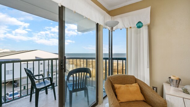 Un balcon avec une chaise, une petite table avec une bougie et une vue sur l’océan.
