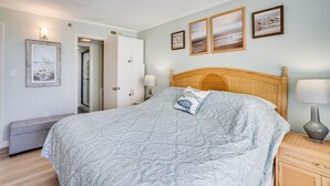 A bedroom with a bed, bedside tables, a bench, and framed pictures on the wall. - Summer Beach 501 by Seaside Vacations & Sales (Ocean City)