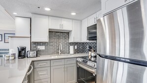 A modern kitchen with grey cabinets, a stainless steel refrigerator, a gas stove, and a black tiled backsplash. - Summer Beach 501 by Seaside Vacations & Sales (Ocean City)