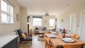 A dining area with a wooden table set for four, a sofa, and a television in the background. - Bethania (Oswestry)