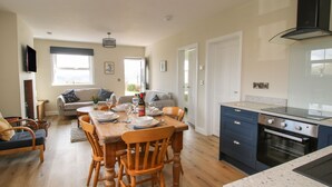 A modern kitchen with a built-in oven and a dining area with wooden chairs and a table set for four. - Bethania (Oswestry)