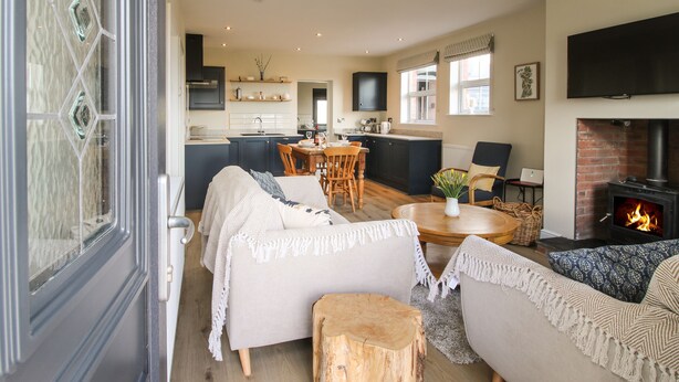 A cozy living room with a fireplace, a dining area, and a kitchen with dark cabinets. - Bethania (Oswestry)
