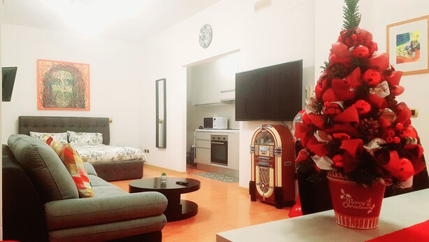 A living room with a sofa, a coffee table, a TV, a kitchen area with a microwave, and a Christmas tree. - Centralissimo e luminosissimo appartamento intero con Open Space. (Taranto)