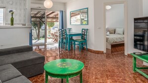 A modern living room with a sofa, a green table, and a dining area with chairs. - Apartamento Adeje con Piscina (Adeje)