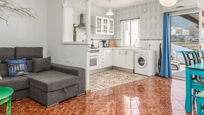 A modern apartment with a grey sofa, a green coffee table, a washing machine, and a dining area with blue chairs. - Apartamento Adeje con Piscina (Adeje)