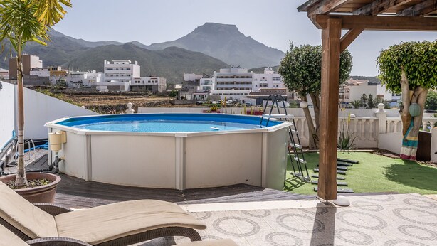 A rooftop pool area with lounge chairs, a wooden pergola, and a view of a mountainous landscape. - Apartamento Adeje con Piscina (Adeje)