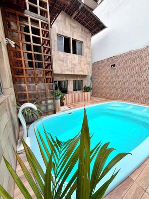 A swimming pool with a wooden deck, a modern house with a patterned facade, and a small garden area. - Casa Porto do Amor (Ipojuca)