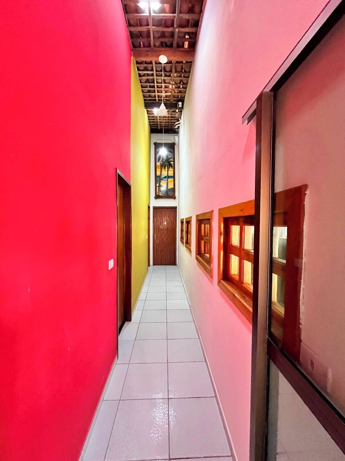 A narrow hallway with tiled flooring, wooden doors, and windows with wooden frames.