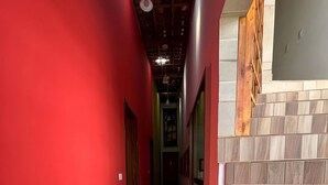 Um corredor com paredes vermelhas, piso de azulejos e escada de madeira.