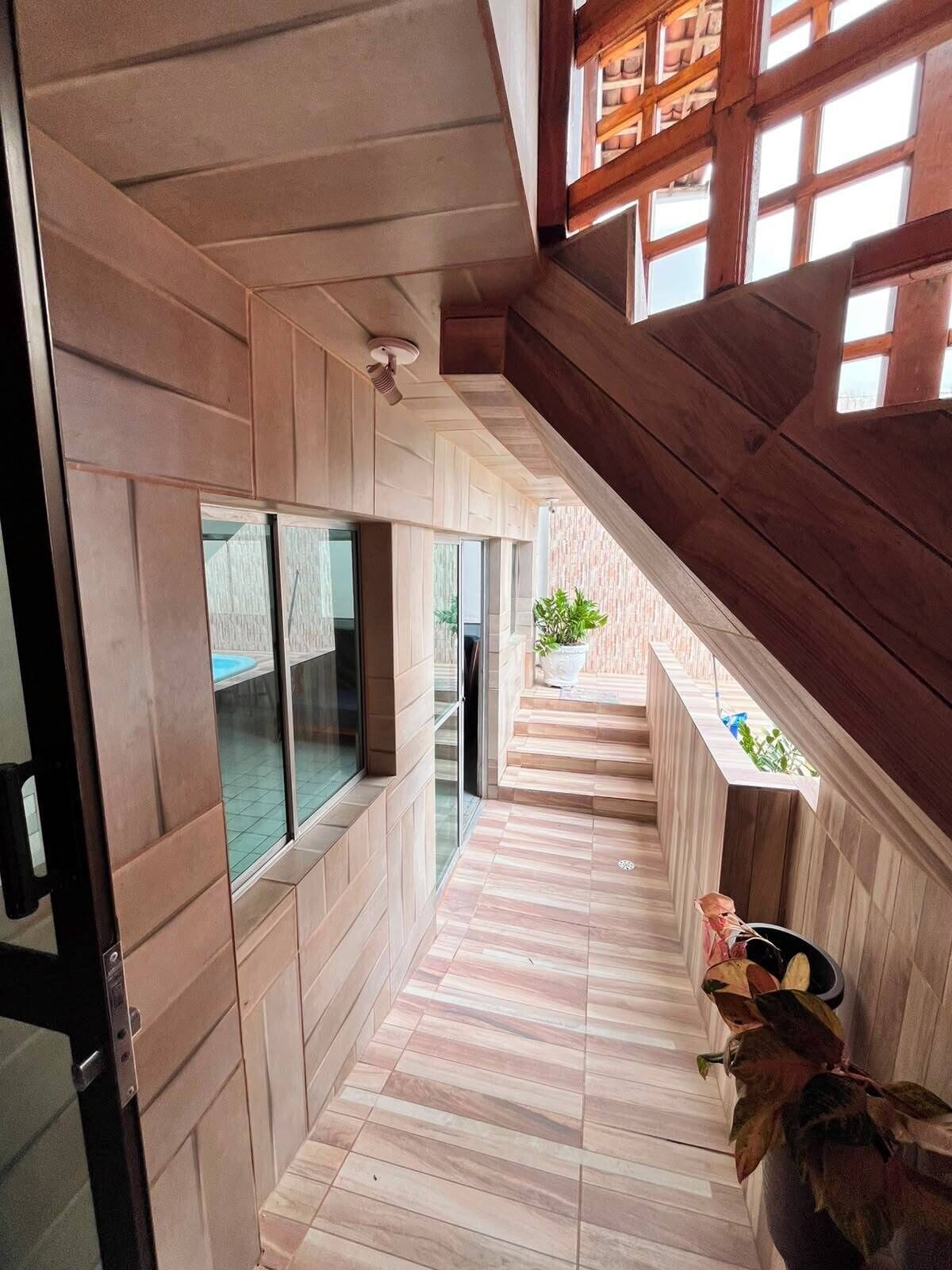 Ein modernes Interieur mit einer Holztreppe, einer Glastür, die auf einen Balkon führt, und einem Topf mit einer Pflanze auf dem Boden.