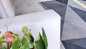 Uma sala de estar com uma televisão de tela grande fixada em uma parede de madeira, um sofá cinza e uma mesinha com uma planta.