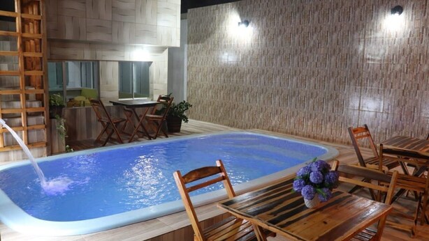 Piscina com cadeiras e mesa de madeira, rodeada por um deck de madeira.