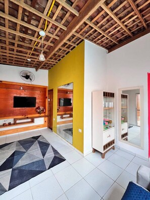 A modern living room with a wooden ceiling, a large TV, a yellow accent wall, and a mirrored cabinet. - Casa Porto do Amor (Ipojuca)