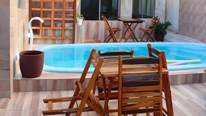 Uma área de piscina com mobiliário de madeira e uma pérgula.