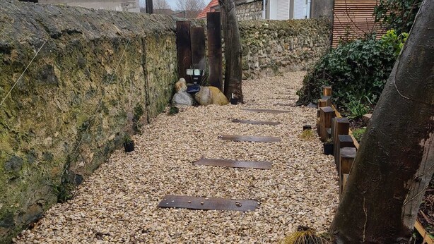 Un sendero de grava con piedras de madera que conducen a un muro de piedra.