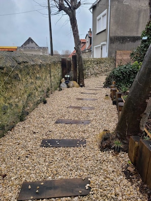 Un chemin de gravier, ponctué de pierres plates en bois, mène à un mur de pierres.