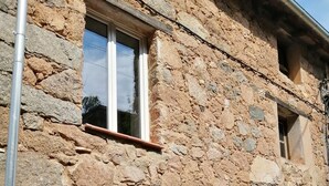 Un bâtiment en pierre avec une fenêtre et des volets, un poteau en métal et une porte.