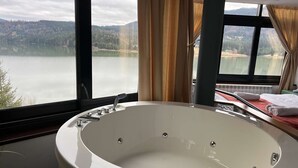 Un baño con una bañera grande, una ventana con cortinas y vistas a un lago y montañas.
