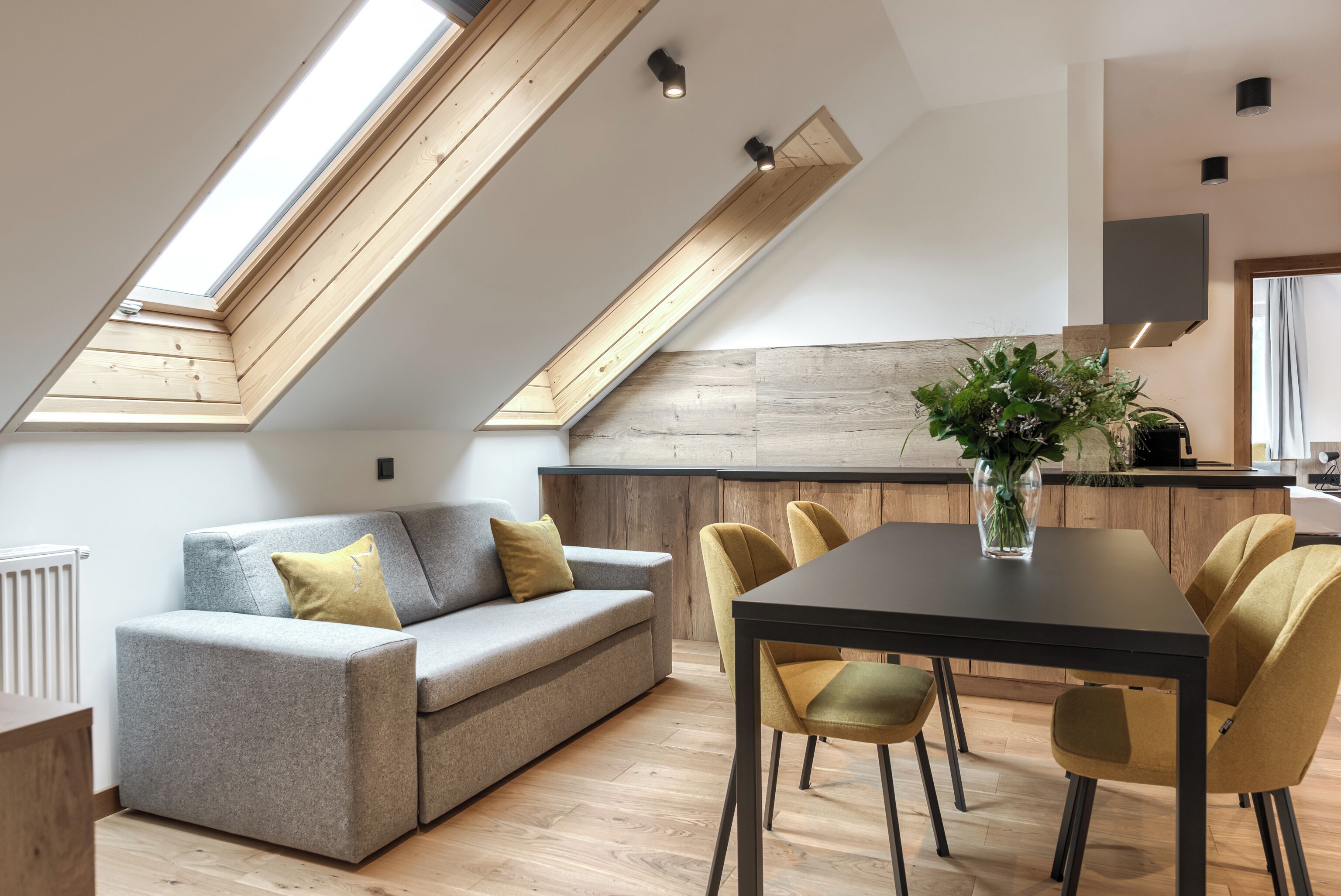 A modern loft with a dining area, a sofa, and a kitchen in the background.