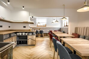 A modern dining area with wooden tables and chairs, a kitchen area with a wooden countertop, and pendant lighting.