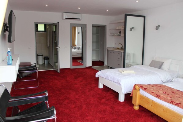 A hotel room with a red carpet, a bed, a desk, a chair, a wardrobe, and a mirror.