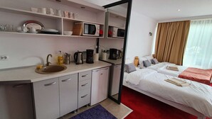 Une chambre d’hôtel compacte comprenant un coin cuisine, un lit avec deux oreillers, une moquette rouge et une fenêtre avec des rideaux.