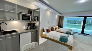 Una habitación de hotel moderna con kitchenette, dos camas, un amplio ventanal con vistas y un pequeño rincón de descanso.