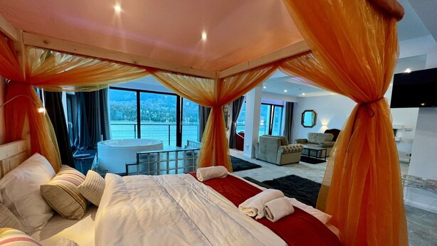 A spacious bedroom with a large bed, a sitting area, and a view of a lake. - Room at lake Colibita with an incredible view over the lake with Jacuzzi. (Colibita)