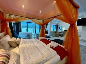 A spacious bedroom with a large bed, a sitting area, and a view of a lake.
