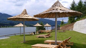 A lakeside outdoor seating area with wooden lounge chairs and thatched umbrellas. - Room at lake Colibita with an incredible view over the lake with Jacuzzi. (Colibita)
