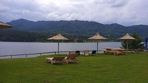 A lakeside outdoor seating area with wooden benches and thatched umbrellas, surrounded by mountains. - Room at lake Colibita with an incredible view over the lake with Jacuzzi. (Colibita)