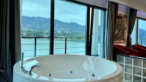A modern bathroom with a large bathtub, a glass shower enclosure, and a view of a lake and mountains. - Room at lake Colibita with an incredible view over the lake with Jacuzzi. (Colibita)