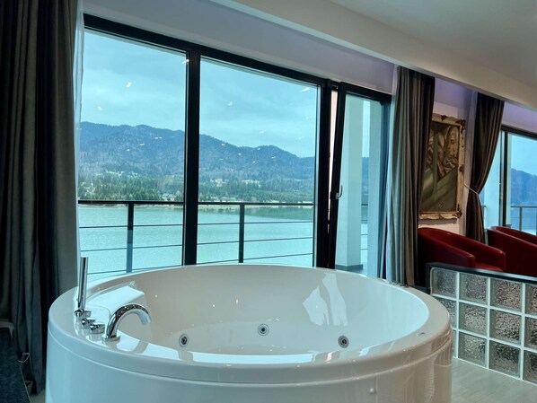 A modern bathroom with a large bathtub, a glass shower enclosure, and a view of a lake and mountains.