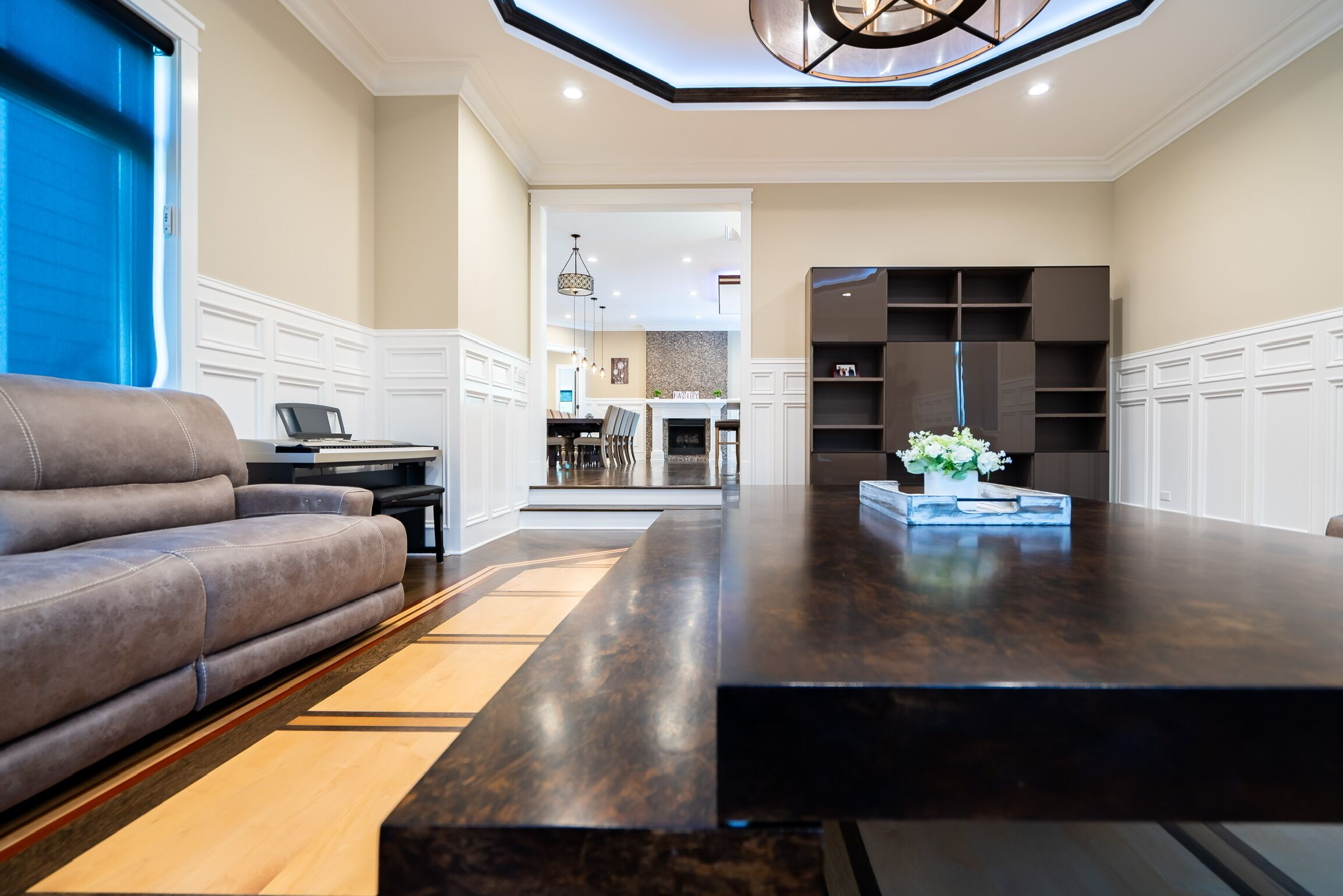 A spacious living room with a dark wooden coffee table, a grey sofa, and a fireplace in the background.
