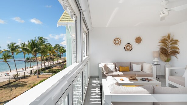 Ein Balkon mit Blick auf den Strand und das Meer, weiße Möbel und dekorative Wandgestaltung.