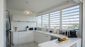Eine moderne Küche mit weißen Schränken, einem Edelstahlkühlschrank, einer Kaffeemaschine und einem großen Fenster mit Jalousien.