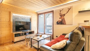 A modern living room with a wooden ceiling, a large flat-screen TV, a leather sofa, and a deer artwork on the wall. - Le Cerf des Alpages - Appt cosy pour 2 (La Giettaz)