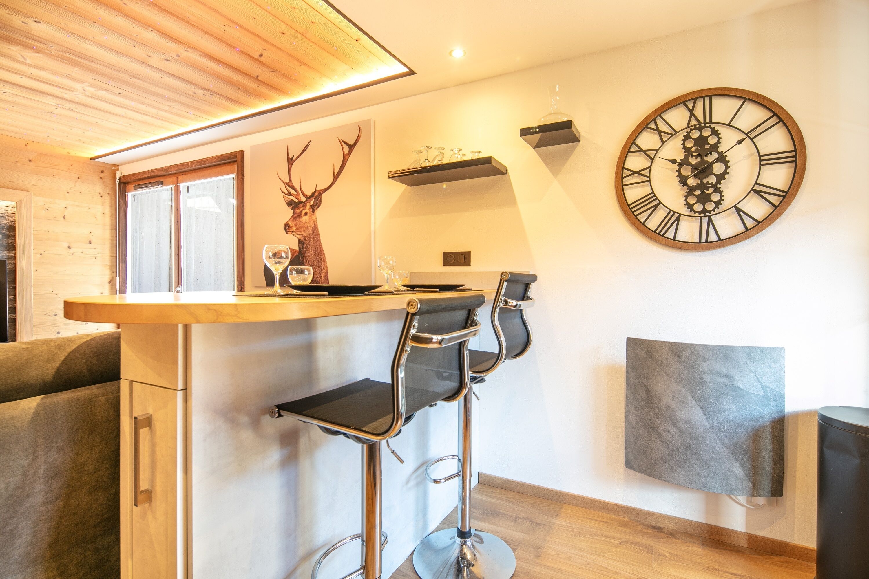 Una cocina moderna con techo de madera, una barra con dos taburetes, un reloj grande y una decoración con cabeza de ciervo.