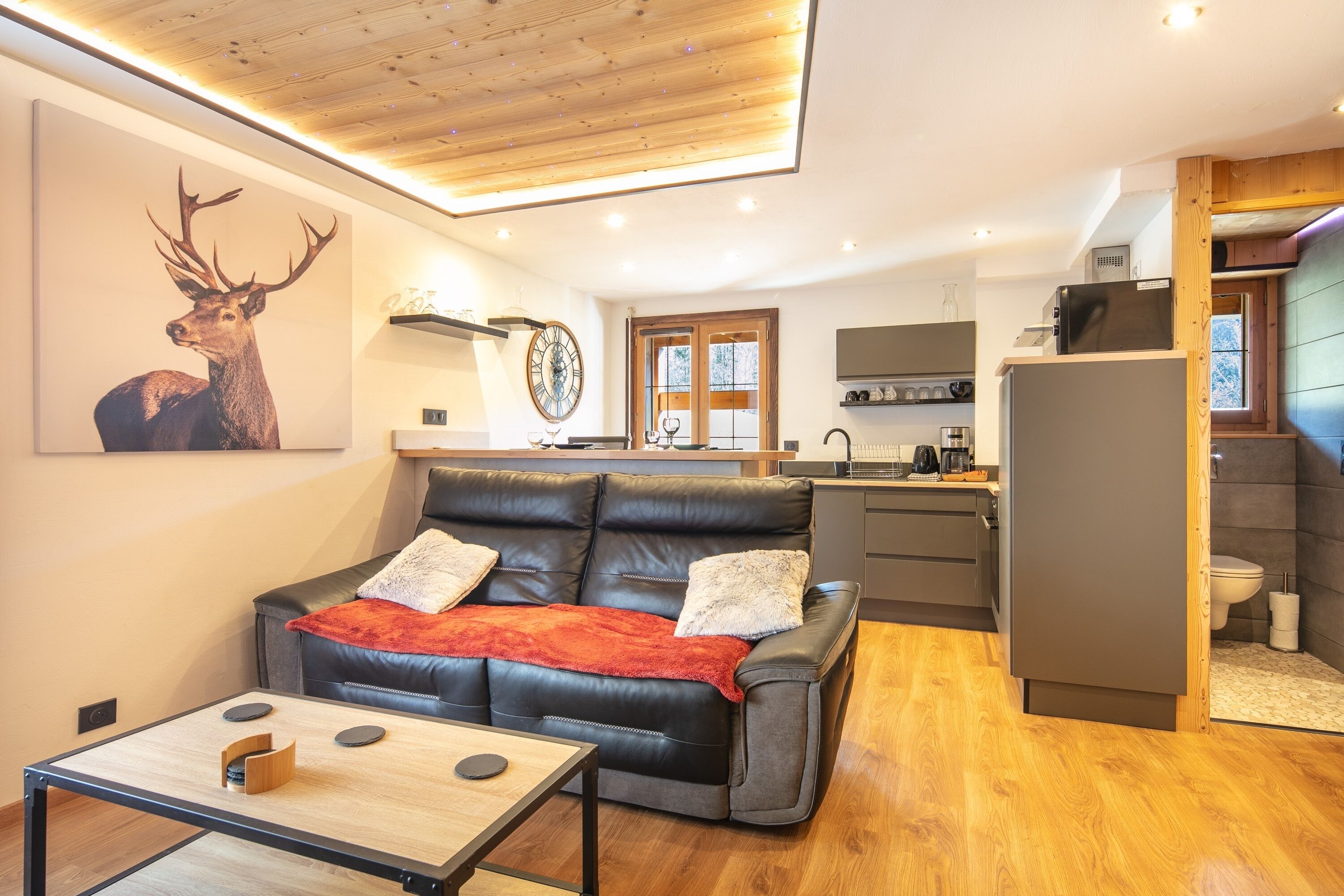 Un salon moderne avec un canapé en cuir, une table basse en bois et une grande œuvre d’art murale représentant un cerf.