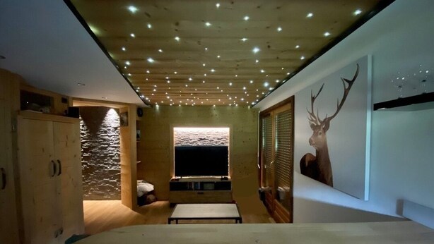 A modern interior with a wooden ceiling, a stone wall, a large window, and a deer mural. - Le Cerf des Alpages - Appt cosy pour 2 (La Giettaz)
