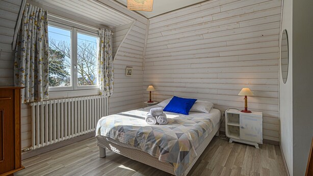 Ein Schlafzimmer mit einem Bett, zwei Nachttischlampen, einem Fenster mit Vorhängen, einer Heizung und einem Holzboden.