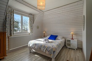 Une chambre à coucher avec un lit, deux lampes de chevet, une fenêtre avec des rideaux, un radiateur et un plancher en bois.