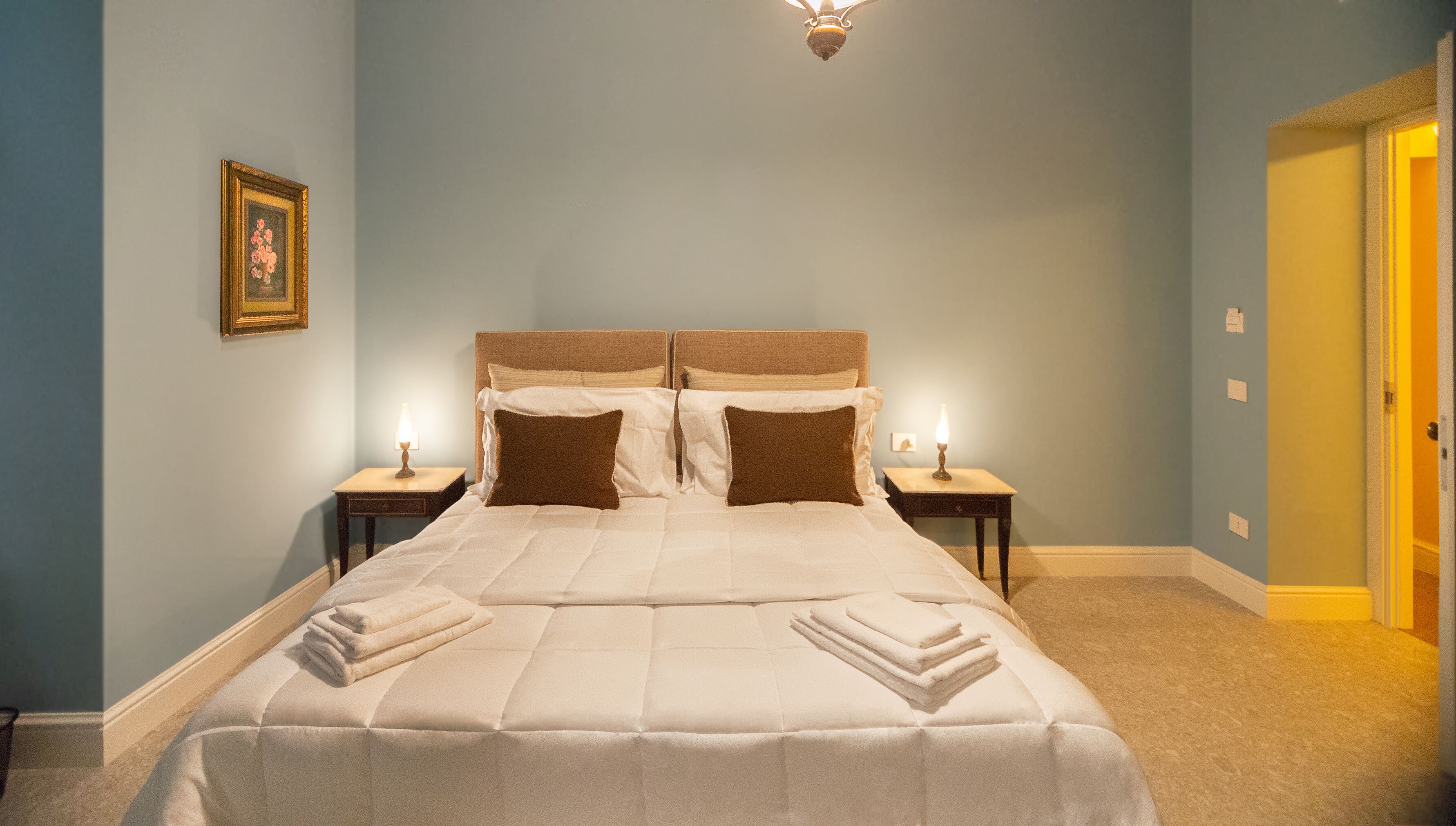 A neatly made bed with a headboard, two bedside tables with lamps, and a framed picture on the wall.